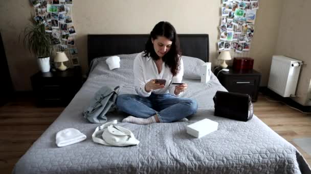 Wanita cantik tersenyum duduk di tempat tidur membeli barang-barang secara online. kartu dan laptop. belanja online. — Stok Video