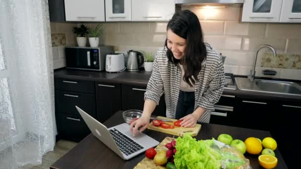 Nő főzés friss saláta vágás paradicsom figyeli recept a laptopon közeli másolás hely — Stock videók