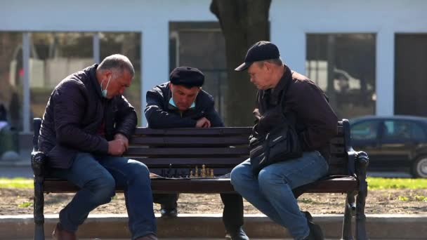 Lviv, Ukraine - 28. April 2021: Senioren sitzen auf der Bank und spielen Schach im öffentlichen Park. Frühling sonniger Tag — Stockvideo