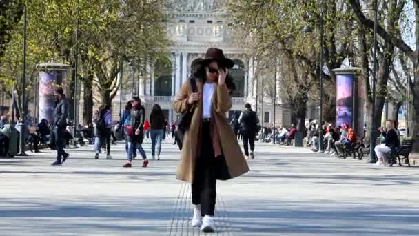 Kahverengi ceketli, güler yüzlü, şık bir kadın sokakta yürüyor. — Stok video
