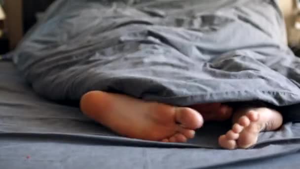 Pareja piernas mujer y hombre bajo la manta gris en la cama — Vídeos de Stock
