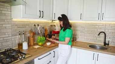 Kadın sandviç yapıyor, adam karısına sarılıyor.