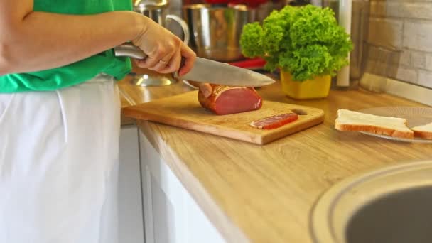 Жінка нарізає м'ясо на різаній дошці на кухні роблячи бутерброди — стокове відео