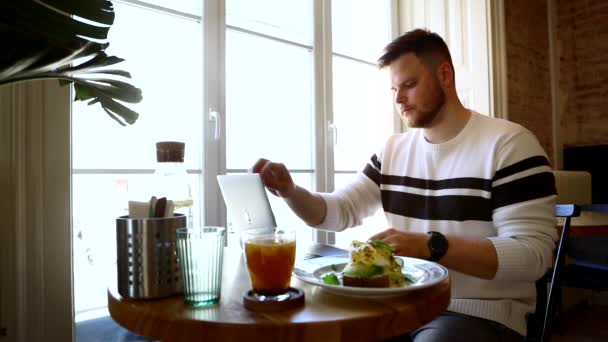 Mann arbeitet an Laptop im Café und isst und trinkt — Stockvideo