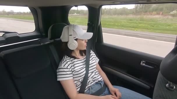 Frau im Fond sitzt angeschnallt mit Sicherheitsgurt und hört Musik — Stockvideo