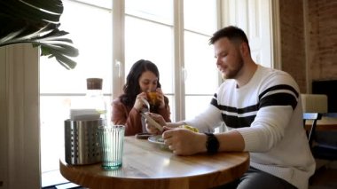 Kafede oturan, içki içen ve yemek yiyen çift büyük pencerenin yanında oturuyor.