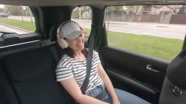 Arkada oturan kadın emniyet kemeriyle kemerini bağlayıp müzik dinliyor.