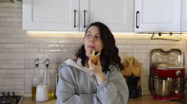 Kadın mutfakta kruvasan yiyor.