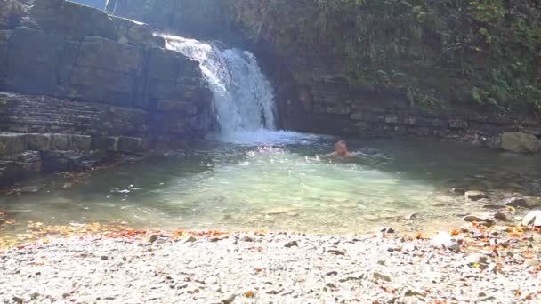 Young strength man swimming in autumn waterfall — Stock Video