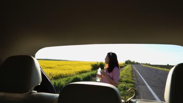 View from car trunk smiling woman sitting and drinking water enjoying view of sunset — Stock Video