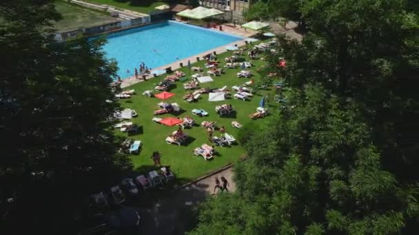 Vista superiore delle persone che prendono il sole sulle sedie a sdraio che nuotano nella piscina della città pubblica — Video Stock