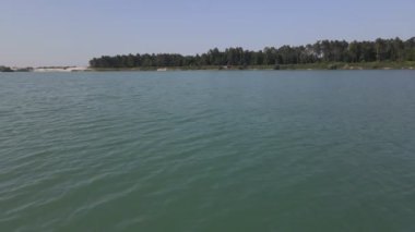 Mavi su gölünün kumlu kumsalında güneşlenen bir kadın.