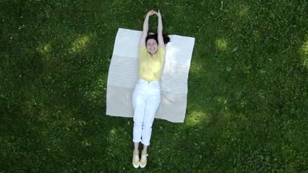 Femme souriante allongée sur la couverture sur l'herbe verte — Video