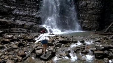 Güzel yürüyüşçü kadın büyük şelalenin önünde duruyor.