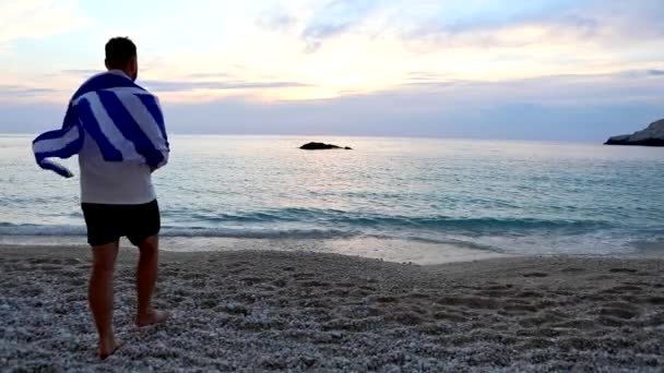 Mann geht am Meer Strand mit griechischer Flagge bedeckt — Stockvideo