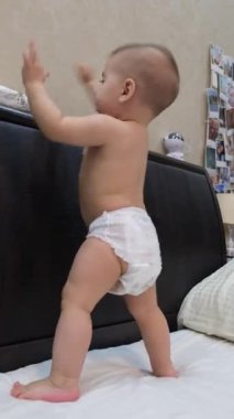 Happy baby learning to stand on bed in diaper