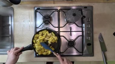 Gaz ocağının tepesinde dilimlenmiş patates pişiriyorum.