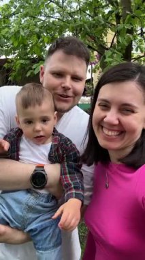 Genç ve mutlu bir aile selfie 'si. Bebek dışarıda kamerada konuşuyor.