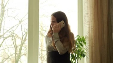 Kız ayakta karşı bir pencere yakınında ve telefonla konuşuyor