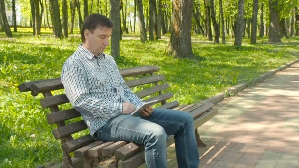 Ernsthafter Mann arbeitet im Park an Tablet-Computer — Stockvideo