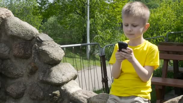 Glücklicher kleiner Junge mit Smartphone im Park — Stockvideo