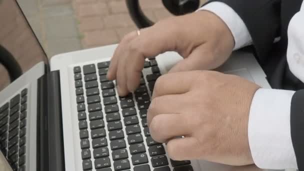 Empresario escribiendo en un portátil y sentado en un banco en la calle — Vídeos de Stock