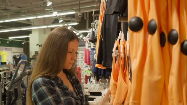 Mooi meisje is het kiezen van kleding in sport winkel in het winkelcentrum — Stockvideo