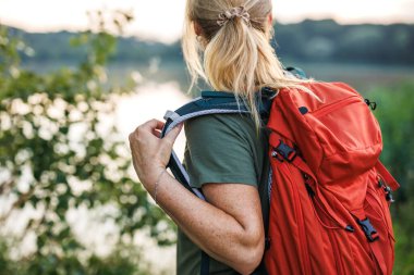 Yürüyüşçü kadın doğa yürüyüşü sırasında kırmızı sırt çantası takar. Kadın turist, açık hava aktivitelerinin keyfini çıkarıyor.
