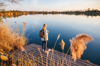Sırt çantalı kadın rıhtımda duruyor ve manzaraya hayran, yavaş yaşam tarzından ve doğayla bağlantısından zevk alıyor.