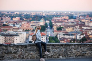 Aşağı kasaba Bergamo 'nun yukarısındaki Venedik Duvarları' nda oturan kadın turist gün batımından sonra Citta Alta 'nın panoramik manzarasının keyfini çıkarıyor. Avrupa 'da şehir arası