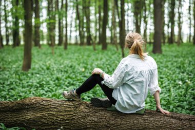 Ormanda yürürken düşmüş ağaç gövdesinde oturup dinlenen bir kadın, sakin bir orman terapisi ve farkındalık anı yaşıyor.