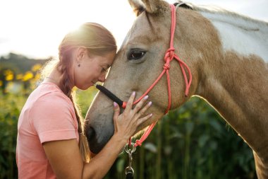 Gülümseyen kadın atıyla bağ kuruyor. İnsanlar ve hayvanlar arasındaki güven, duygusal bağ ve dostluğu gösteriyor. At destekli terapi.