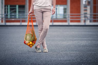 Şehirde alışveriş yaptıktan sonra tekrar kullanılabilir ağ torbası tutan kadın. Sıfır atık ve plastiksiz sürdürülebilir yaşam tarzı