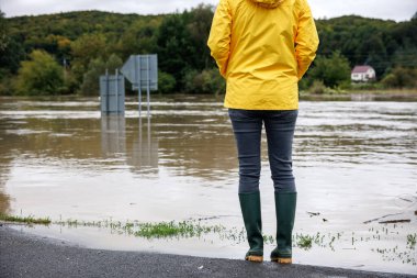 Şiddetli yağmurdan sonra sel. Sel basmış nehre bakan endişeli bir kadın. Aşırı hava ve doğal afet