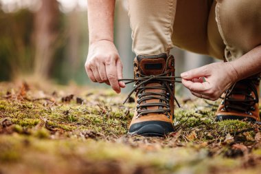 Yürüyüş ayakkabısına ayakkabı bağı bağlayan bir kadın. Turist ormandaki yürüyüş parkurunda yürüyüşe hazırlanıyor.