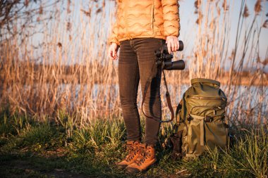 Göl kenarında kuş gözlemi. Dürbünü ve sırt çantasıyla sazlığın arkasında duran kuşbilimci.