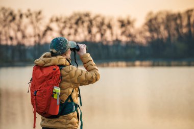 Kuş izleme ve yaban hayatı gözlemi. Dürbünlü kadın gün batımında gölde hayvan ve kuş arıyor.