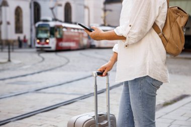 Sokakta tramvayı bekleyen bavulu ve akıllı telefonu olan bir kadın turist. Şehirde toplu taşıma araçlarıyla seyahat