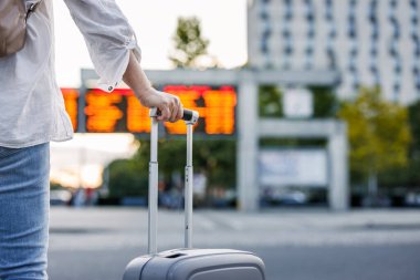 Tatilde seyahat etmek. Valizli kadın yolcu, tren ve otobüs duraklarındaki varış ve kalkış çizelgesini kontrol ediyor.