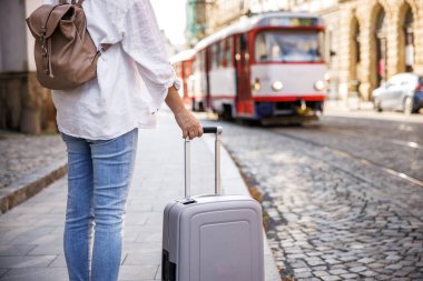 Sokakta tramvayı bekleyen valiz ve sırt çantalı bir kadın turist. Şehirde toplu taşıma araçlarıyla seyahat