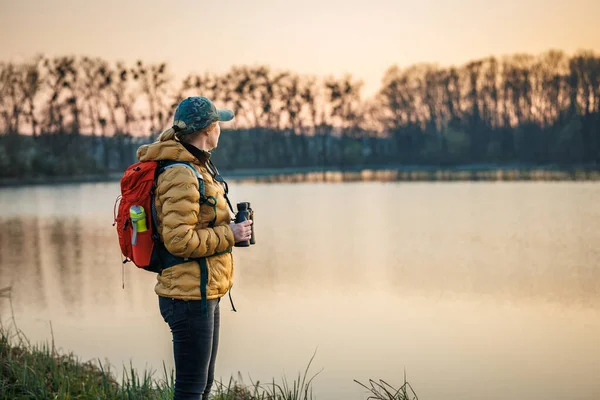 Gün batımında kuş gözlemciliği. Dürbünlü kadın gölde vahşi hayvan ve su kuşu arıyor.
