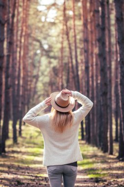 Kadın doğada güneş ışığının ve temiz havanın tadını çıkarıyor. Ormanda örülmüş kazak ve şapka giyen Boho kadını.