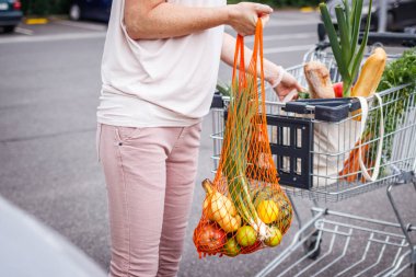Kadın tekrar kullanılabilir ağ torbalarını araba bagajına yüklüyor. Sıfır atık ve plastik ücretsiz alışveriş