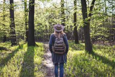 Ormanda yürüyüş. Baharın güneşli bir gününde şapkalı ve sırt çantalı bir kadın dışarıda yürüyüş yapıyor.