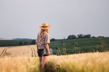 Çiftçi hasat zamanından önce tarla tarımı yapıyor ve inceliyor. Hasır şapkalı ve dijital tabletli kadın arpa tarlasında duruyor.
