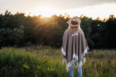 Günbatımında, ruh sağlığı ve kendi iyiliği için doğada dinlenen kadın.
