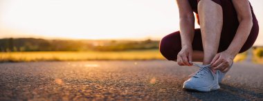 Koşu ayakkabılarına ayakkabı bağı bağlayan bir kadın. Gün batımında yolda koşmadan önce hazırlık. Spor ve spor aktiviteleri