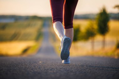 Yolda koşan spor ayakkabılı bir kadın. Açık hava fitness ve spor eğitimi