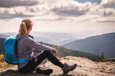 Dağ yürüyüşü sırasında rahatlama. Sırt çantalı bir kadın kayanın üzerinde oturuyor ve manzaranın tadını çıkarıyor. Dağ zirvesinde turist yürüyüşü ve tırmanışı