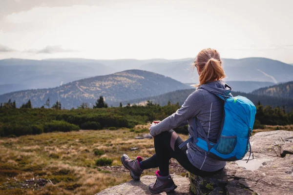 Dağ yürüyüşü sırasında rahatlama. Sırt çantalı bir kadın kayanın üzerinde oturuyor ve manzaranın tadını çıkarıyor. Dağ zirvesinde turist yürüyüşü ve tırmanışı